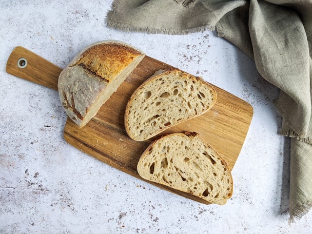 A sourdough loaf cut open on a wooden board beside a linen cloth, showing an open, irregular crumb